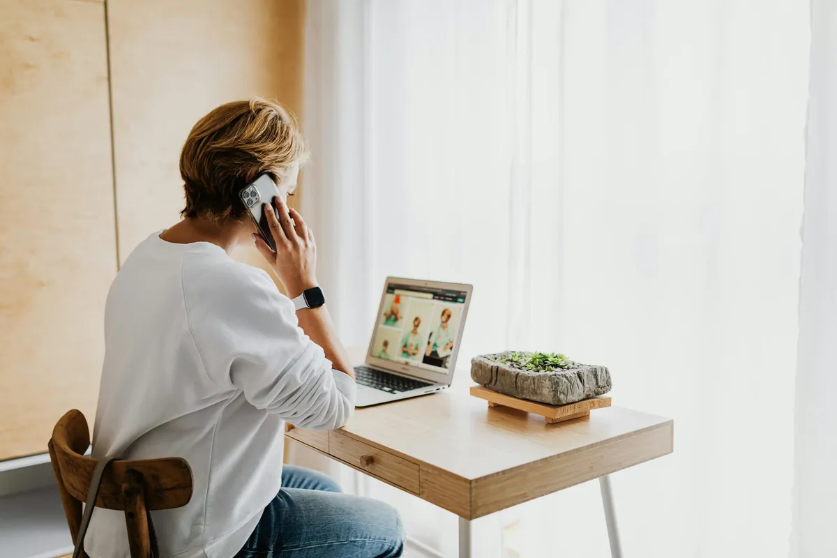 A person on a video call using a laptop and smartphone at a home desk